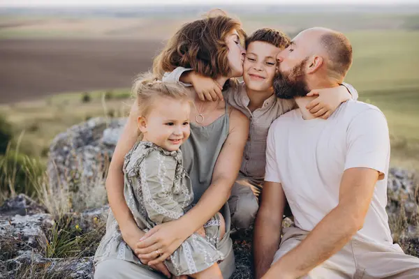 A smiling couple sitting closely together on a couch, gently holding a newborn baby in their arms. Both adults are looking down at the baby with warm, affectionate expressions, creating an intimate and tender family moment in a softly lit home setting.